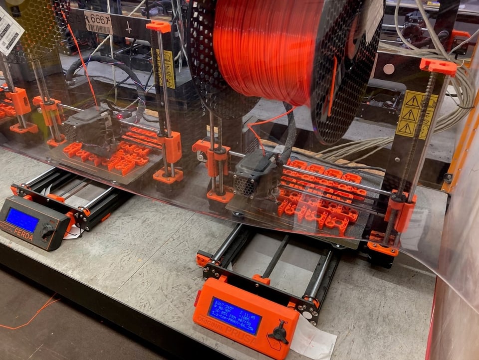 Ein 3D-Drucker druckt mehrere Teile aus orangem Plastik.