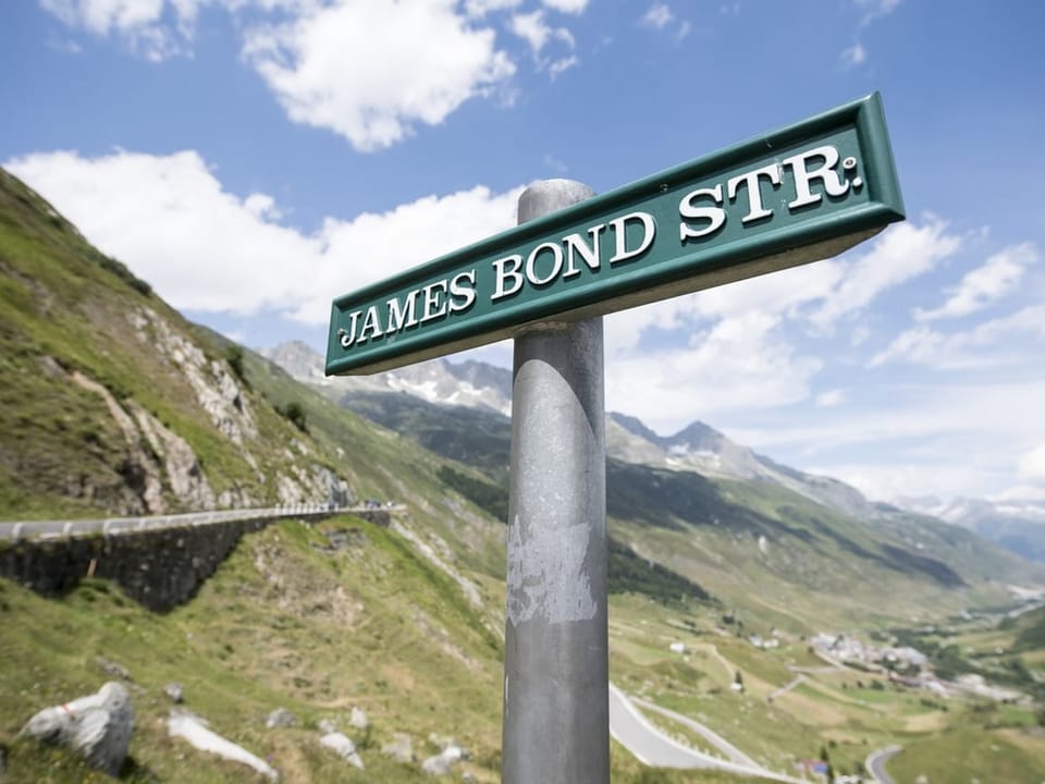 Strassenschild der 'James Bond Str.' in bergiger Landschaft.