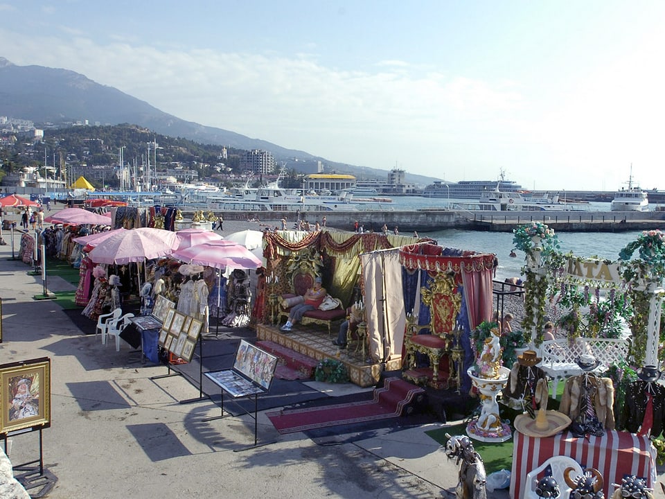 ein bunter Trödelmarkt bei Sonnenschein und blauem Himmel an der Uferpromenade. 