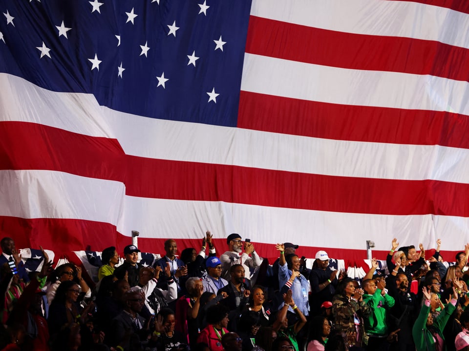 Menschen vor grosser USA-Flagge.