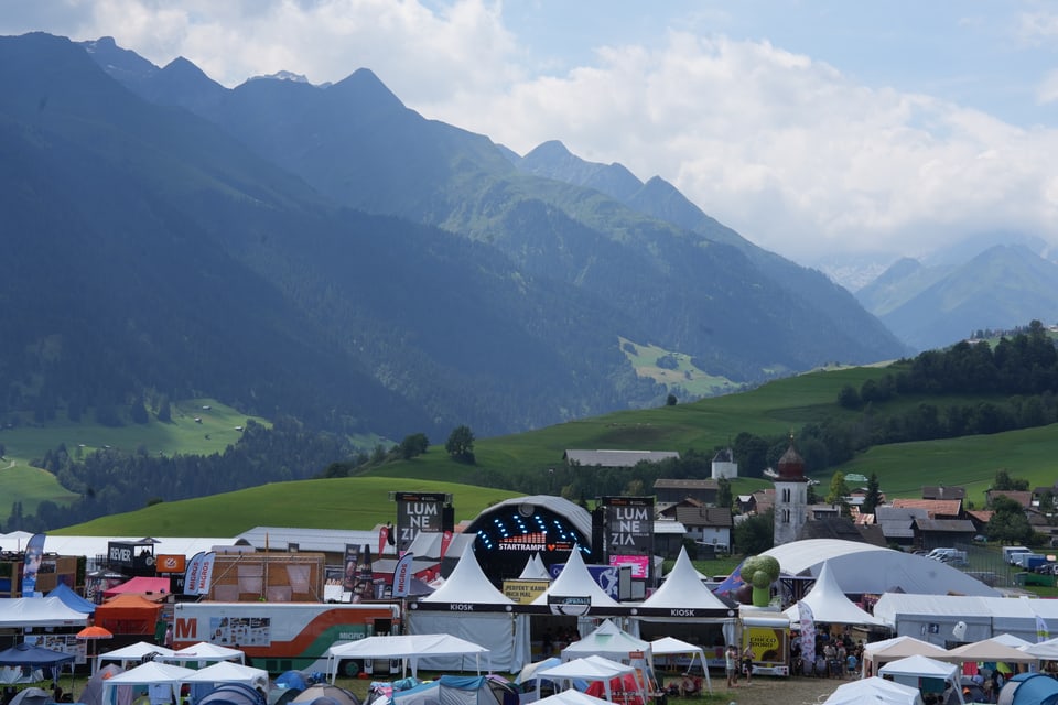 Festivalgelände mit Bergen im Hintergrund am Open Air Lumnezia 2024.