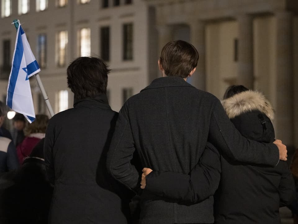 Personen von hinten im Freien, eine hält eine Flagge.