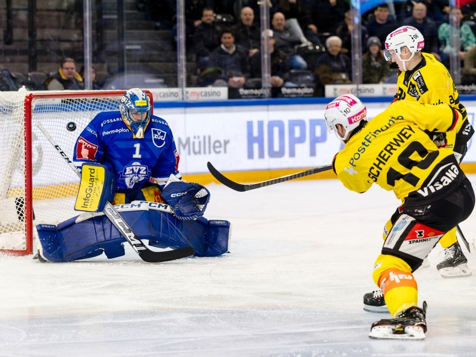 Eishockeytorwart in blauer Ausrüstung pariert Schuss von Spieler in gelbem Trikot.