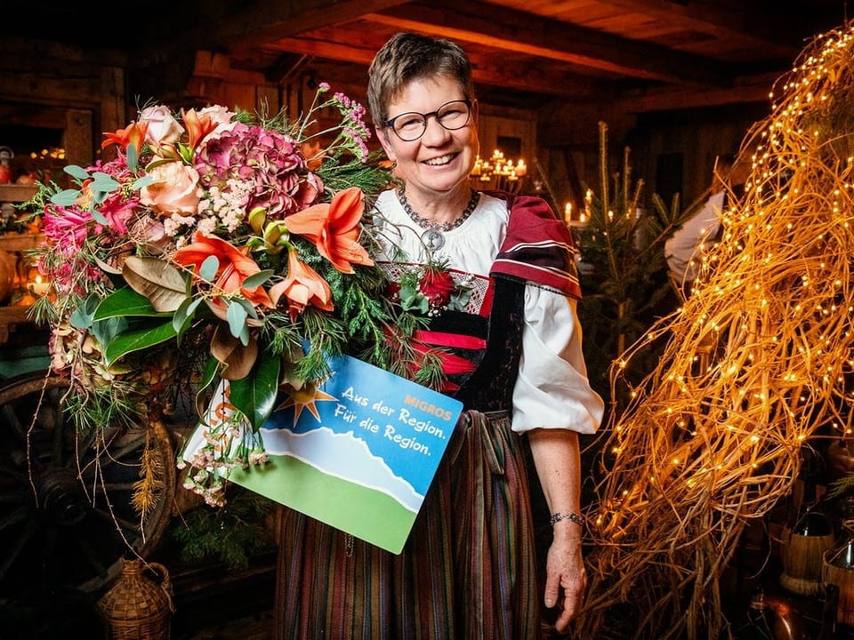 Eine Frau in Schweizer Tracht posiert für ein Foto mit einem grossen Blumenstrauss in ihrer rechten Hand.