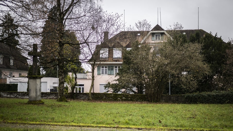 Totale auf ein Gebäude – im Vordergrund ein steinernes Kreuz.