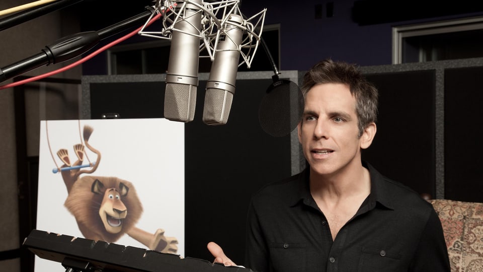 Der Schauspieler Ben Stiller steht in einem Synchronstudio vor zwei Mikrofonen.