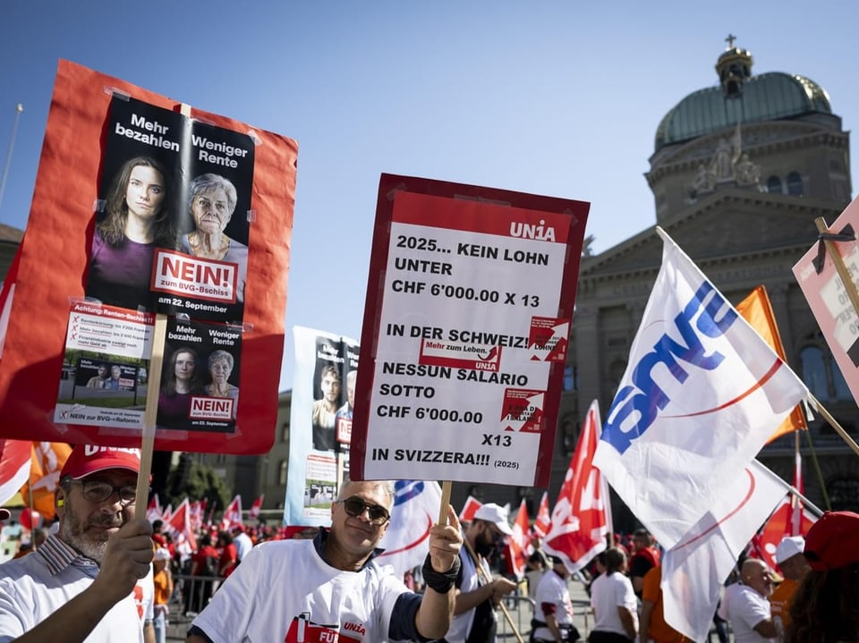 Menschen mit Schildern protestieren vor einem Gebäude.