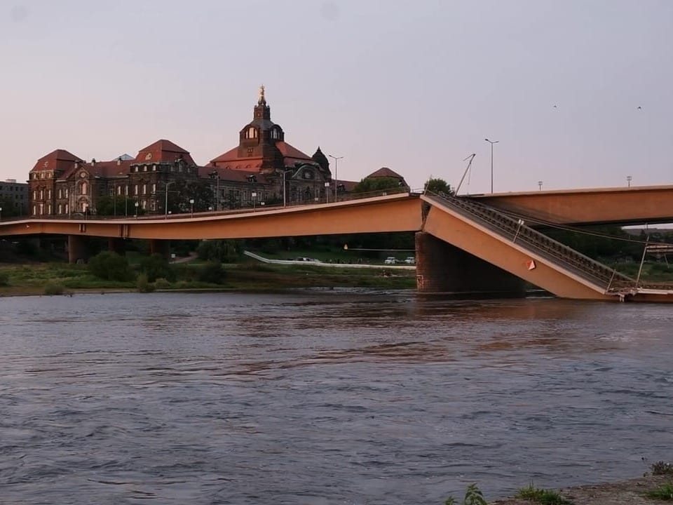 Fluss mit Brücke und Gebäuden im Hintergrund bei Sonnenuntergang.