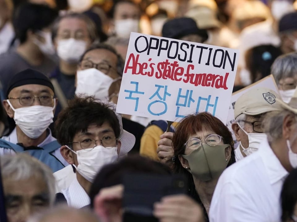 Menschen protestieren auf einer Strasse in Japan und halten Schilder in die Höhe.
