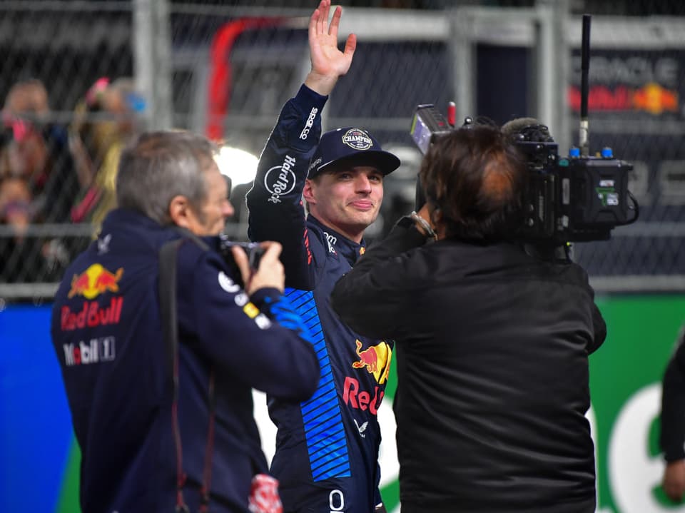 Rennfahrer in Red Bull-Jacke winkt bei Kamerainterview.