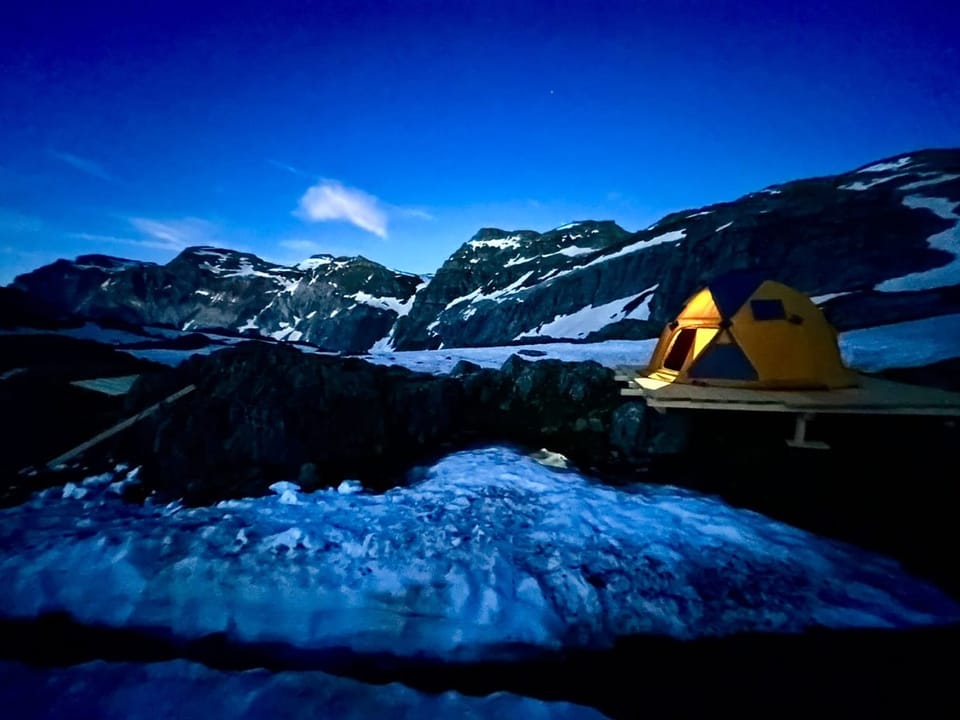 Ein gelbes Zelt in einer Berglandschaft, es ist fast dunkel.