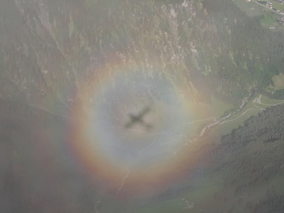 Flugzeugschatten in Regenbogen über Landschaft.