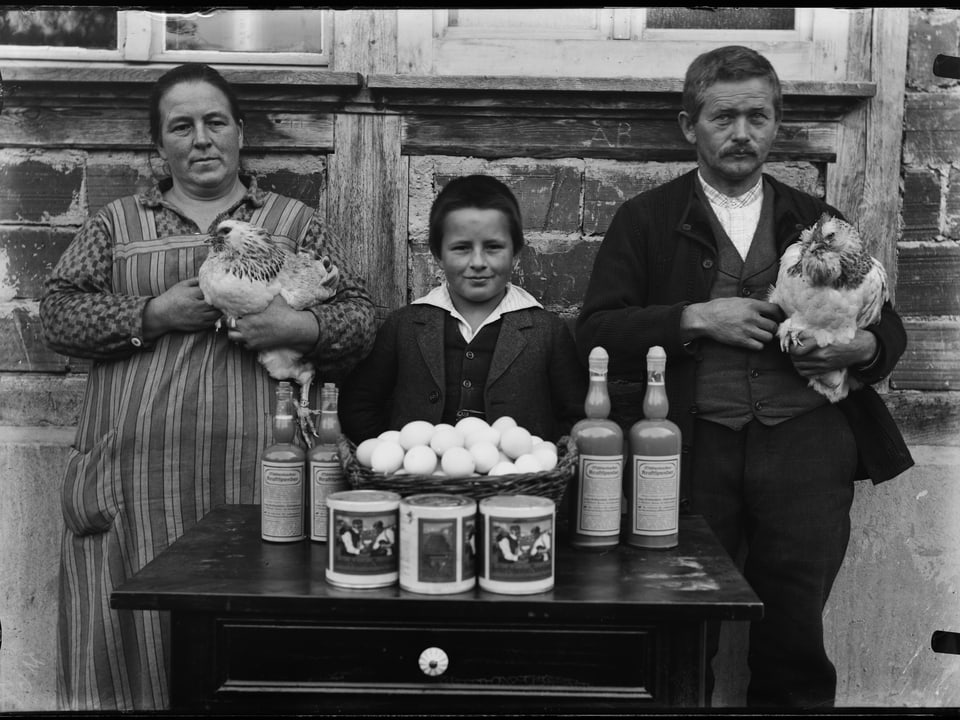 Historisches Bild mit dreiköpfiger Familie hinter einem Tisch mit Eiern und Honigdosen.