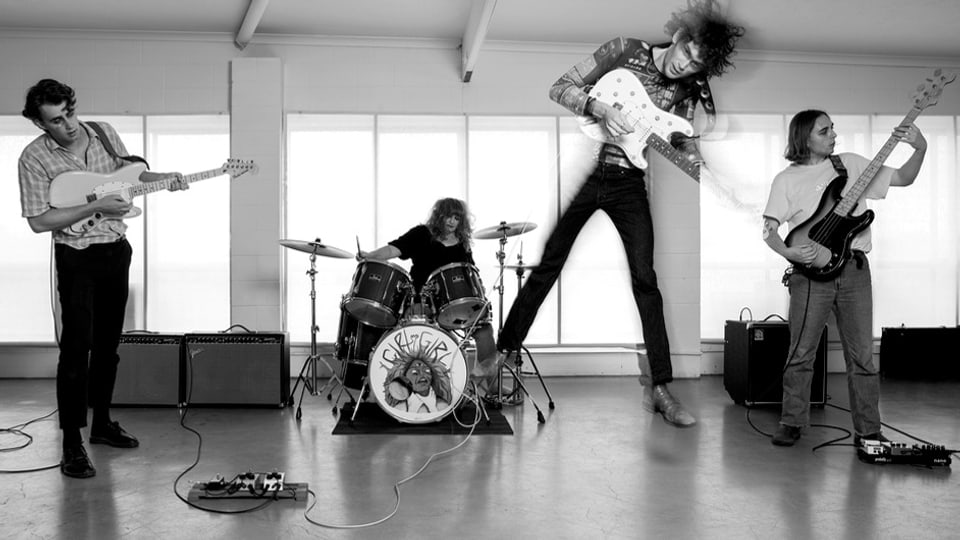 Schwarzweissfoto: Eine Musikgruppe, der Lead-Gitarrist springt in die Luft. 