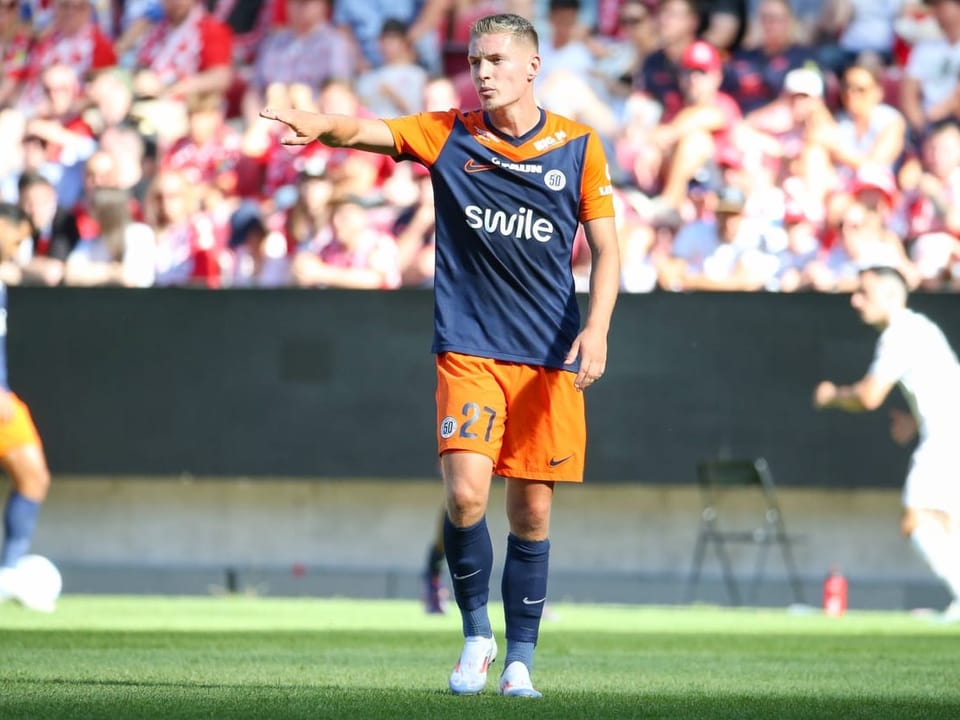 Fussballspieler im orange-blauen Trikot zeigt auf dem Spielfeld.