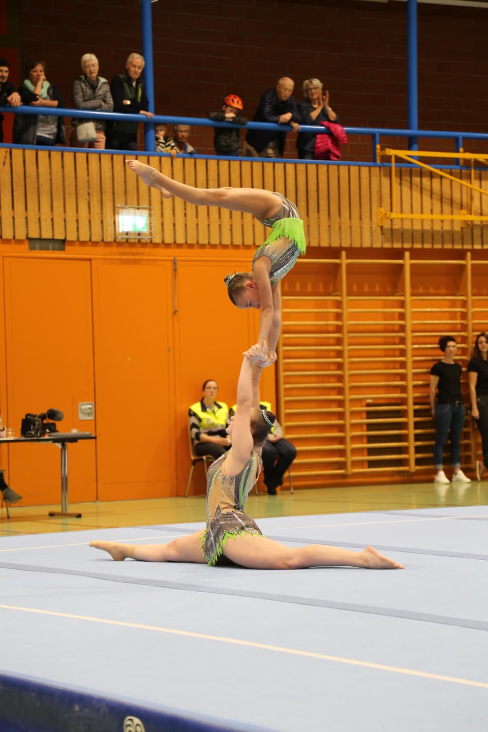 Zwei Turnerinnen bei einer Akrobatikvorführung in einer Sporthalle.