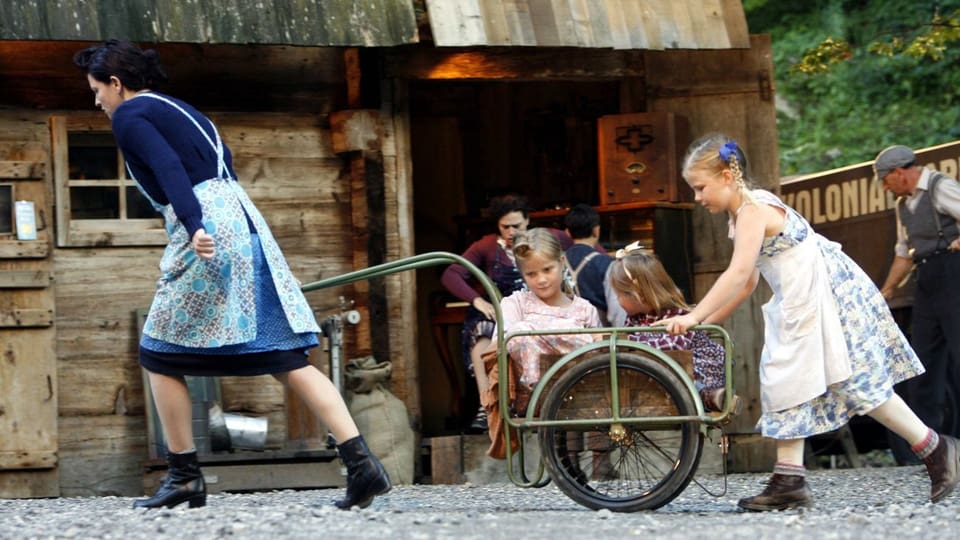 Szene aus dem «Schwarzen Tanner», aufgeführt im Freilichtmuseum Ballanberg: Eine Frau zieht einen Velo-Anhänger, darin zwei Mädchen, ein drittes Mädchen stösst den Anhänger.