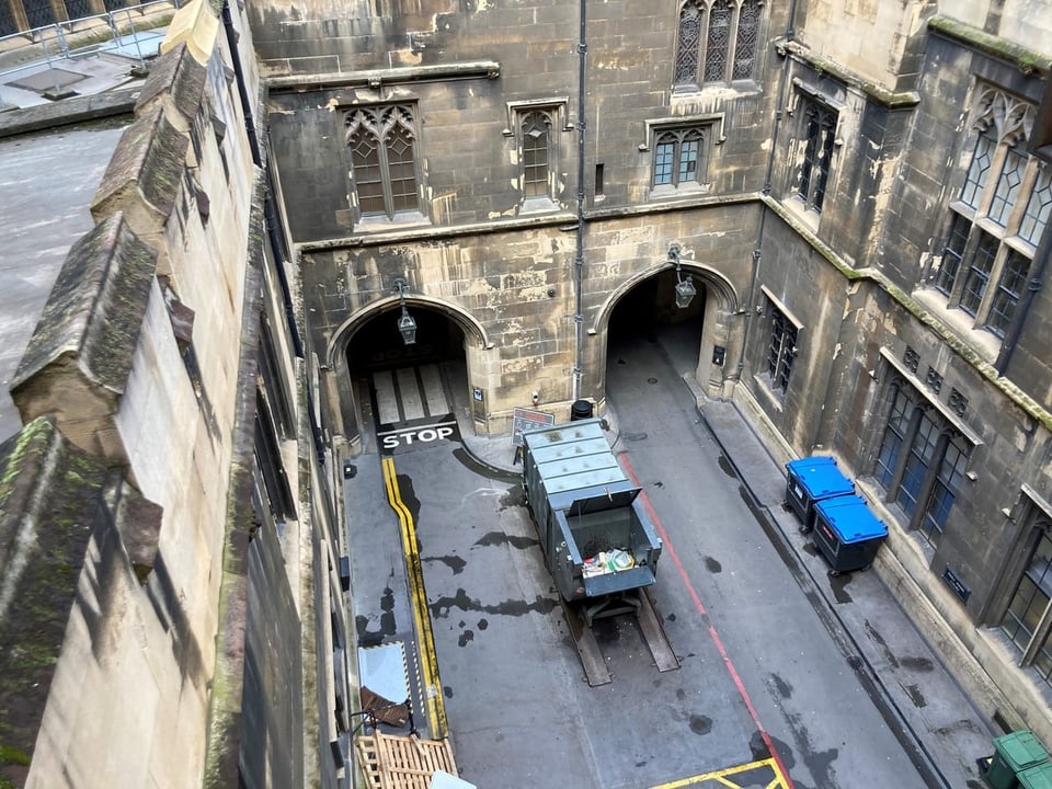 View from the top of the courtyard of an old building with archways and parked vehicles.