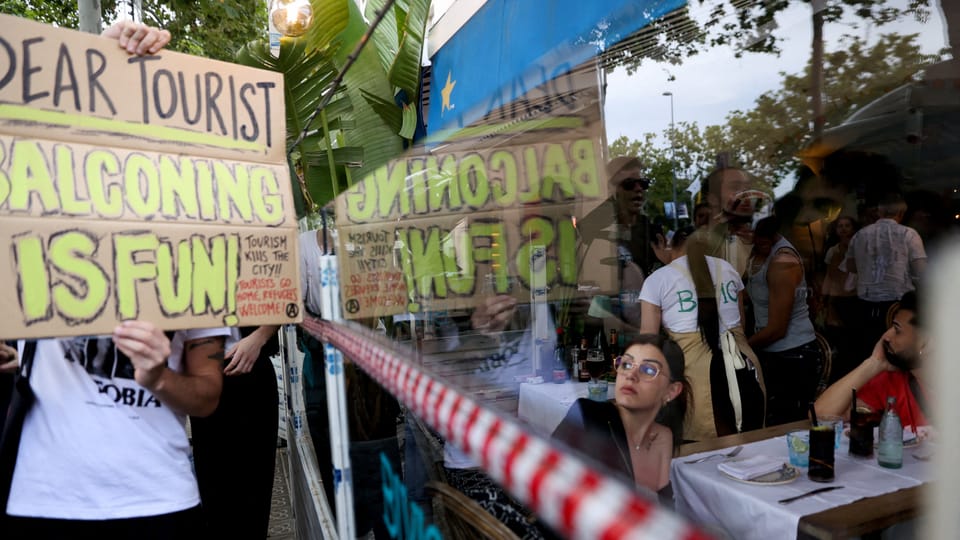 Personen mit Schildern, die gegen 'Balconing' protestieren; Spiegelung im Restaurantfenster.