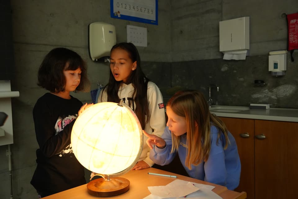 Drei Kinder betrachten zusammen einen leuchtenden Globus.