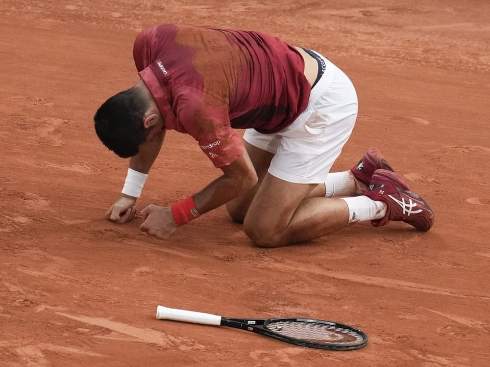 Tennisspieler kniet auf rotem Sandplatz neben Schläger.