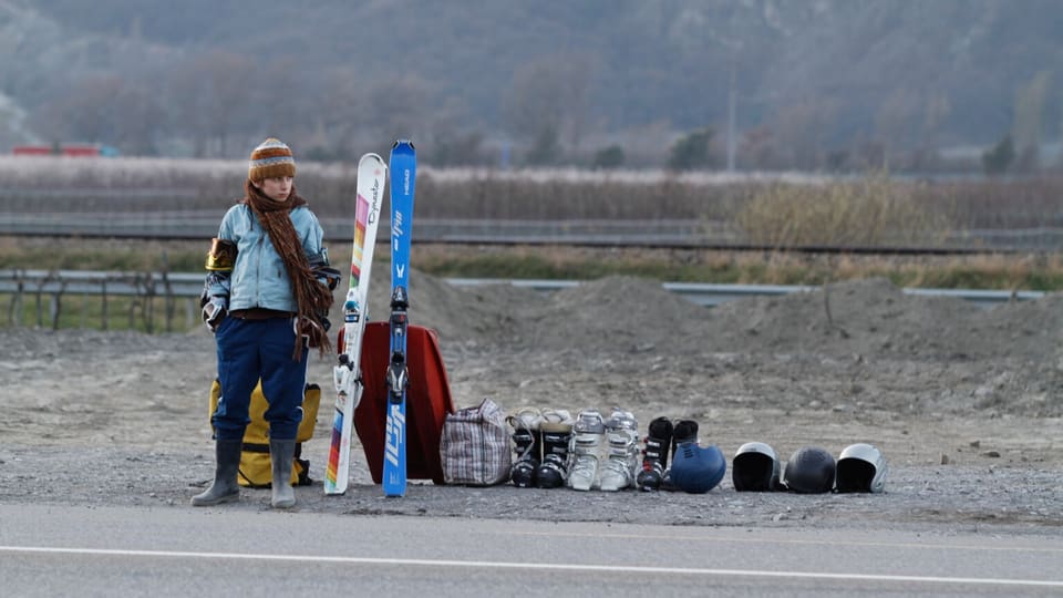 Ein junger Mann steht mit geklauter Skiausrüstung auf einer Strasse.