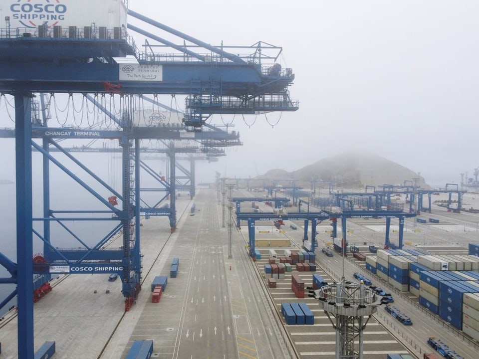 Nebeliger Hafen mit grossen blauen Kränen und Containern.