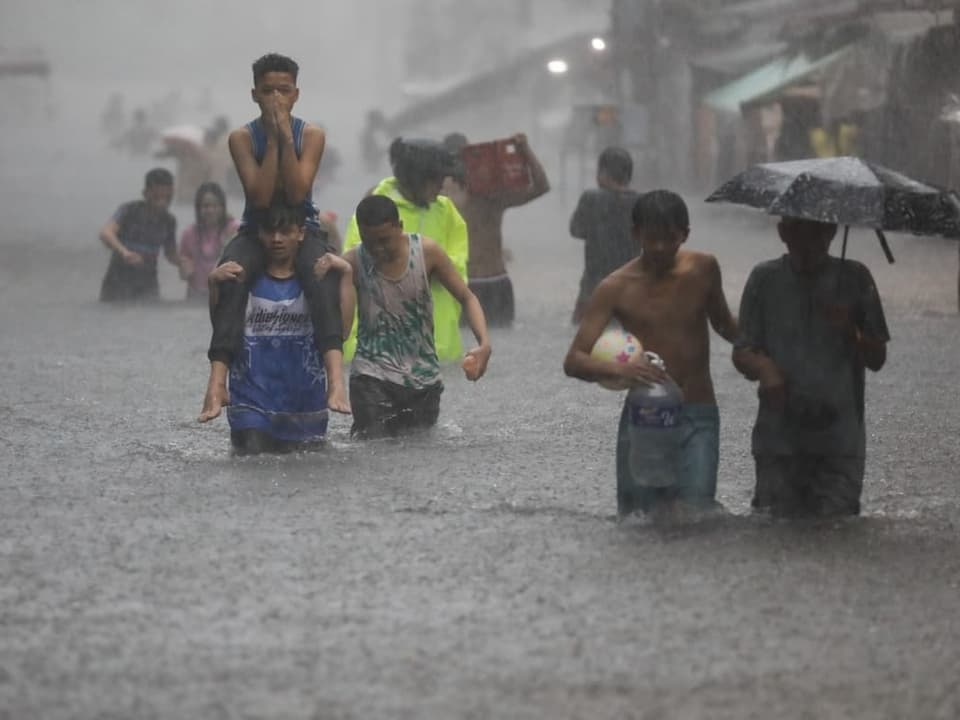 Menschen waten durch eine überflutete Strasse im Regen.