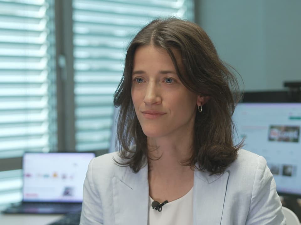 Frau in Büro mit Laptop im Hintergrund.