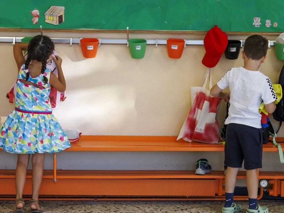 Zwei Kinder hängen Rucksäcke in der Garderobe auf.