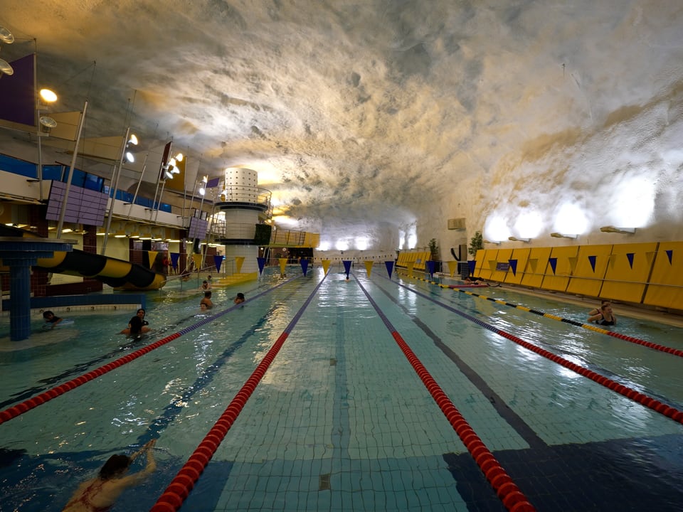 Grosses Hallenbad mit Wasserrutsche und schwimmenden Menschen.