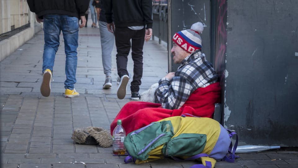 Bettler sitzt auf Trottoir, Leute gehen an ihm vorbei