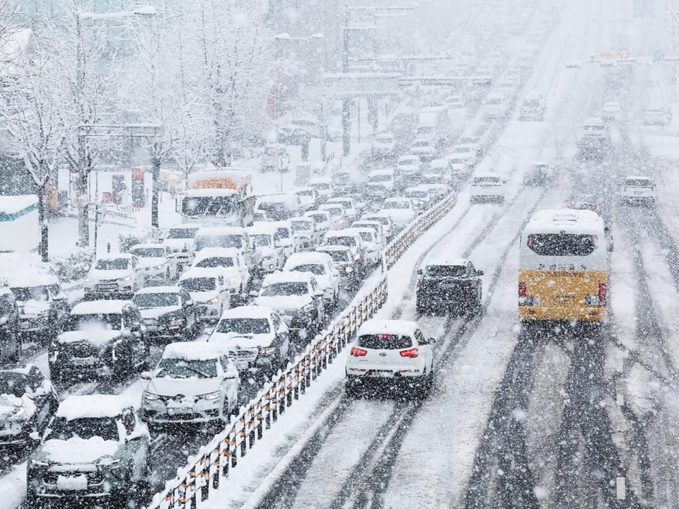 Auf der linken Fahrspur stehen viele Autos im Stau auf den Schneebedeckten Strassen.