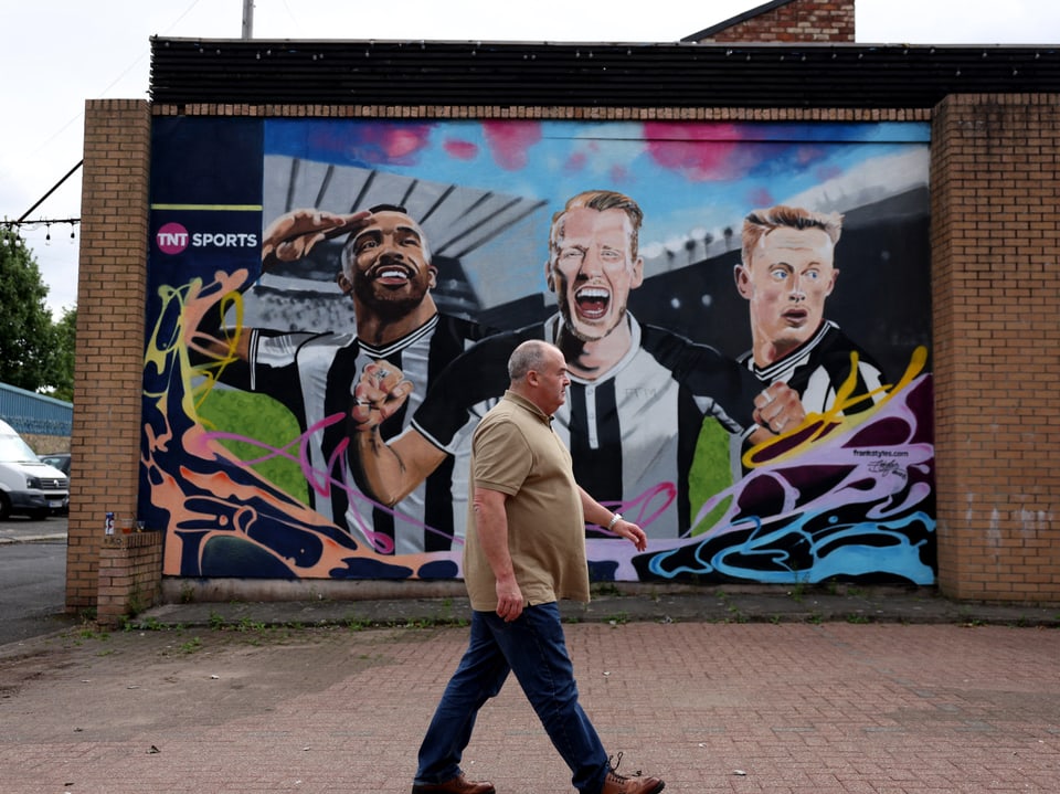 Graffiti von drei jubelnden Fussballspielern auf einer Wand.