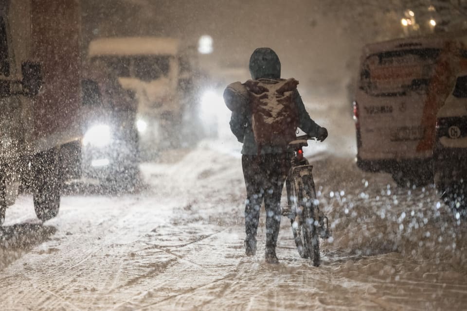 Person schiebt Fahrrad durch Schneesturm auf vereister Strasse.