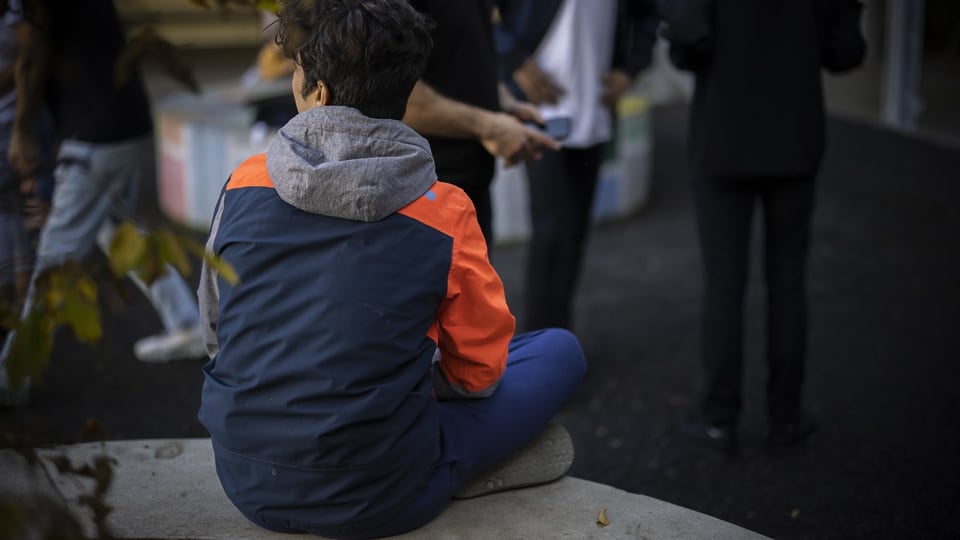 Junger Flüchtling von hinten  – sitzend.