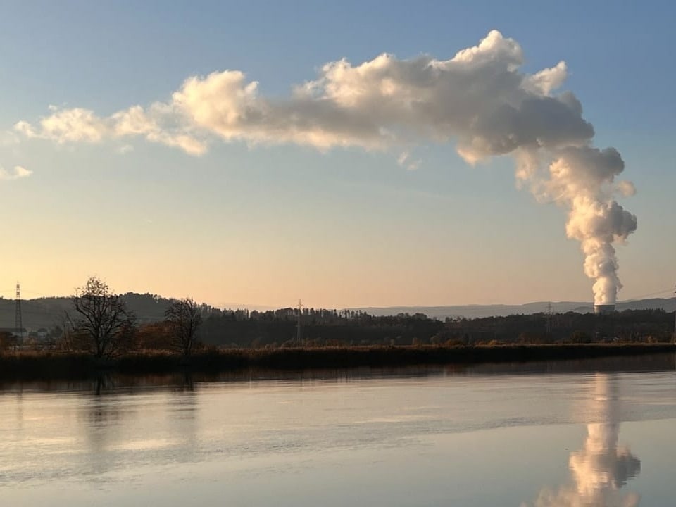 Industrieanlage mit rauchendem Schornstein an einem Seeufer.