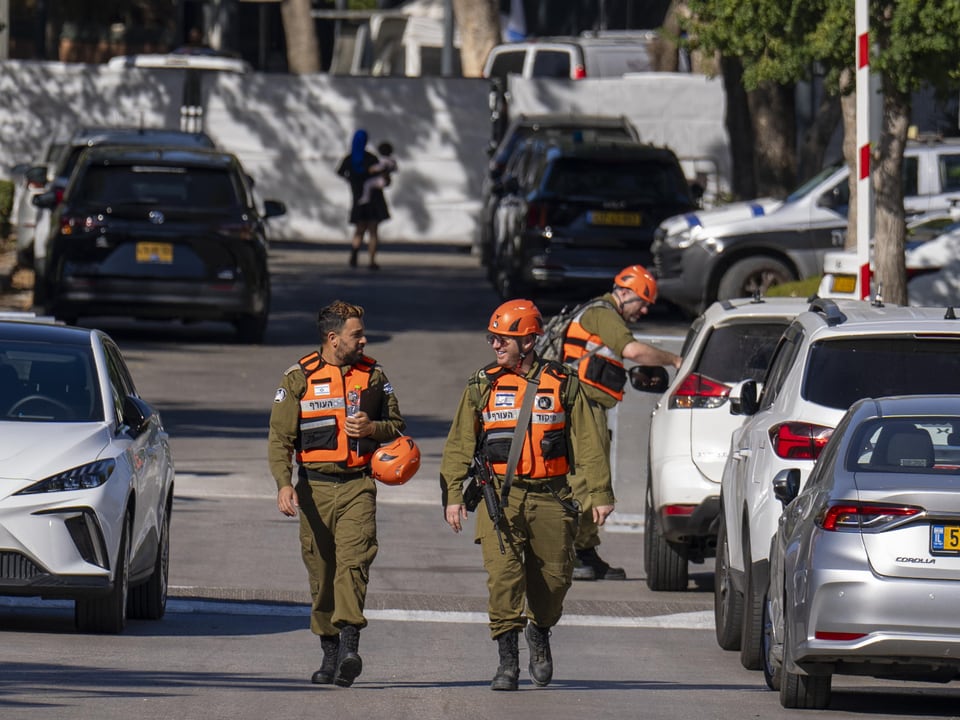 Drei uniformierte Personen mit orangefarbenen Westen auf einer Strasse zwischen Autos.