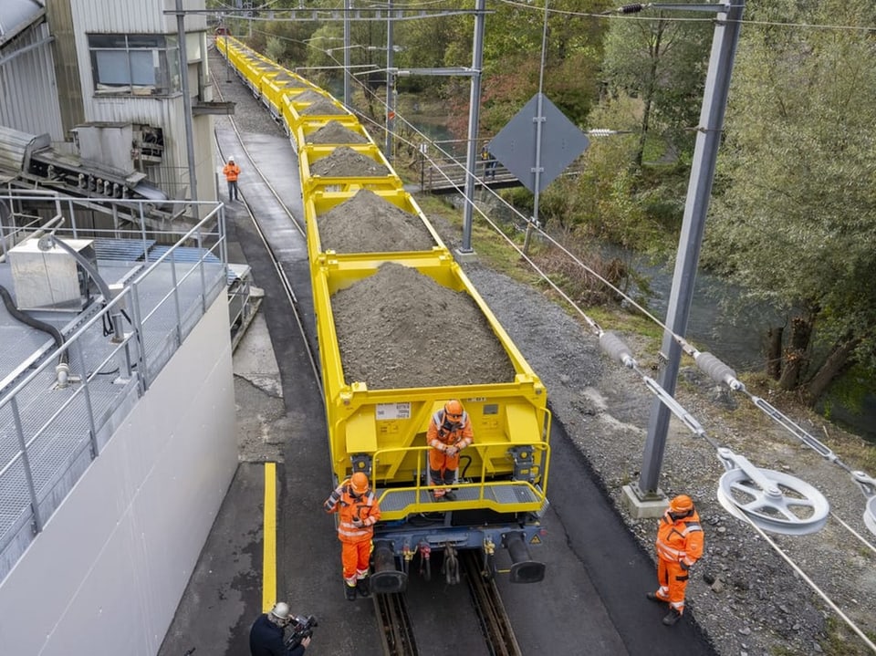 Arbeiter in orangefarbener Arbeitskleidung auf Güterzug mit Kies.