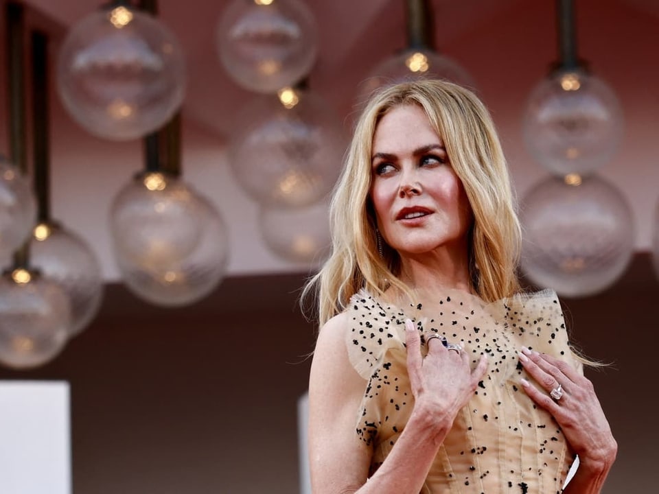 Nicole Kidman mit blondem Haar in einem dekorativen Kleid unter runden Lichtern.