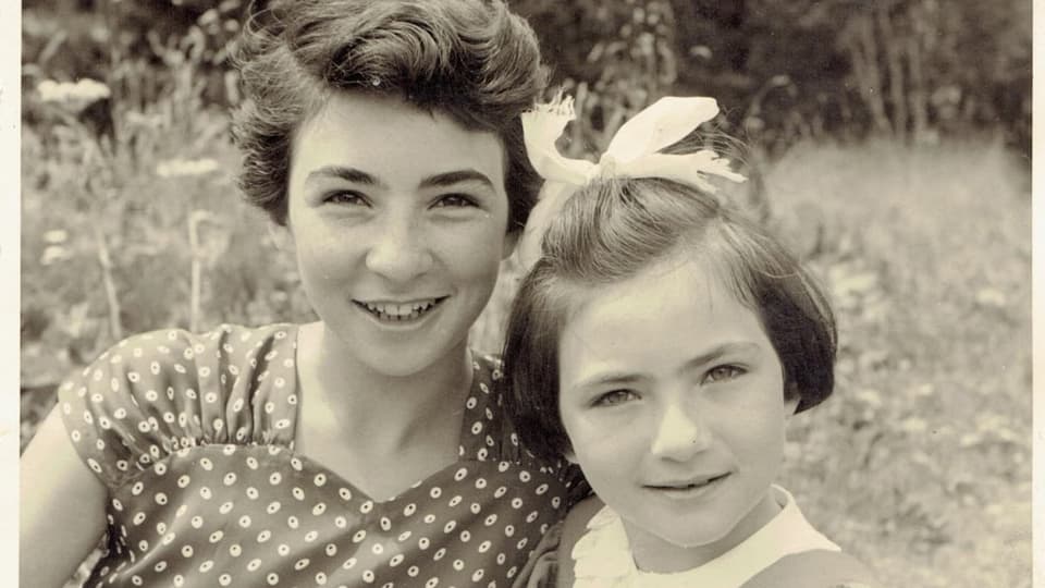 schwarzweiss-Bild von zwei Mädchen auf einer Wiese, links ältere mit dunklem Haar, rechts jüngere mit Haarschlaufe