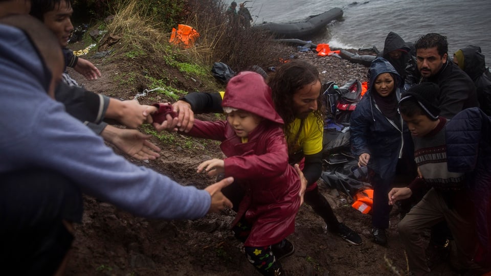 Zwei Männer helfen einem kleinen Mädchen eine Böschung hinauf, hinten weitere Bootsflüchtlinge am Ufer.