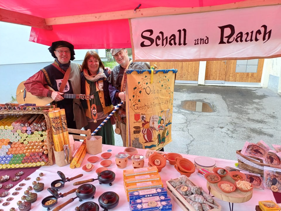 Menschen in historischer Kleidung hinter einem Marktstand mit Handwerksprodukten.