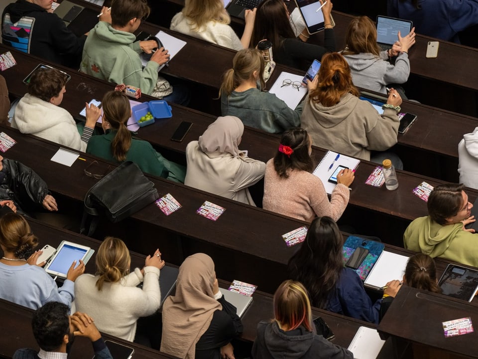 Studierende in einem Hörsaal mit Tablets und Notizblöcken.