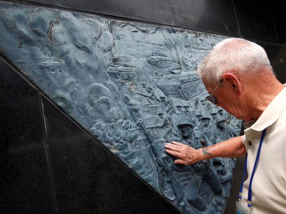 Person berührt ein Relief an einem Gedenkstein.