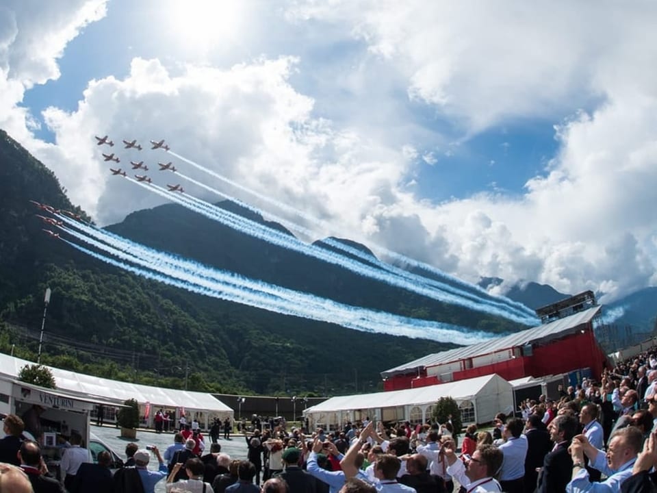 Zwei Formationen der Patrouille Suisse fliegen über eine Menschenmenge, im Hintergrund Berge.