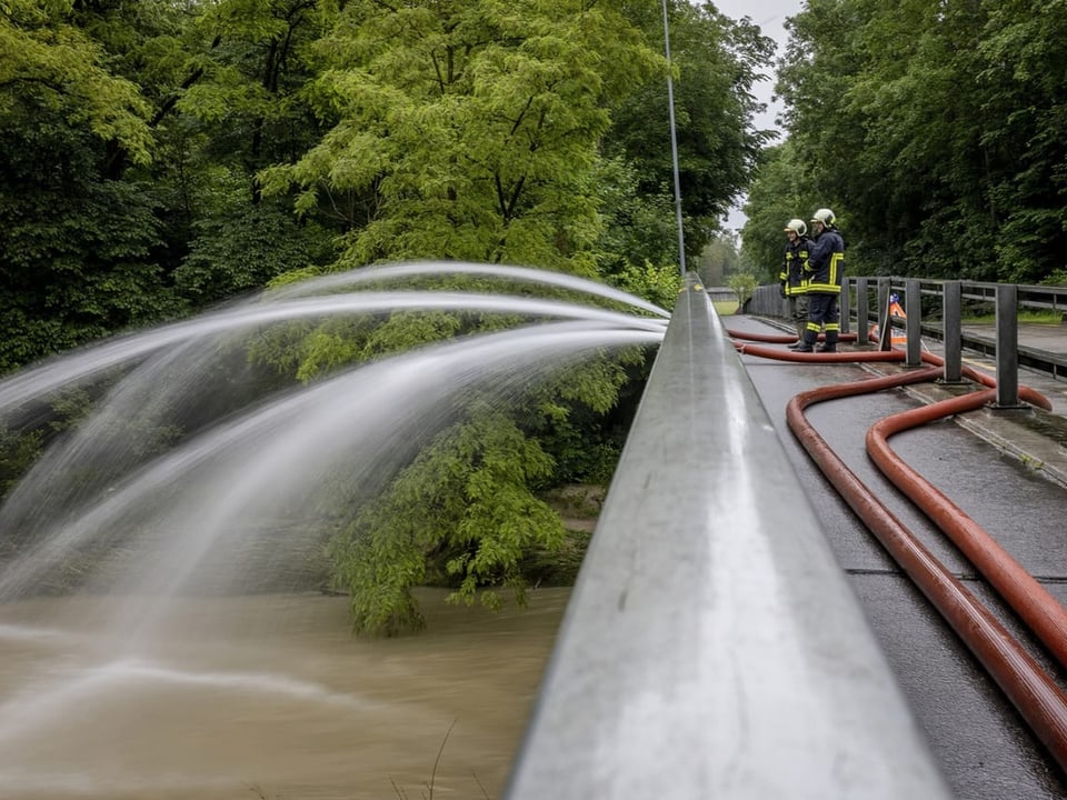 Feuerwehrleute spritzen Wasser von Brücke in Fluss.