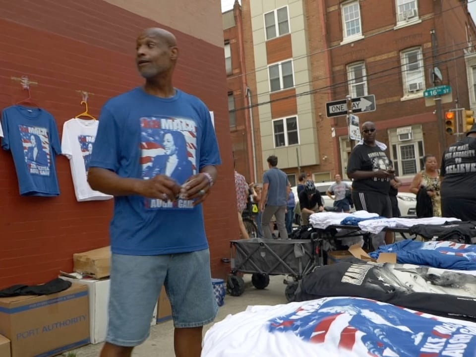 Person verkauft T-Shirts auf einem Strassenmarkt.