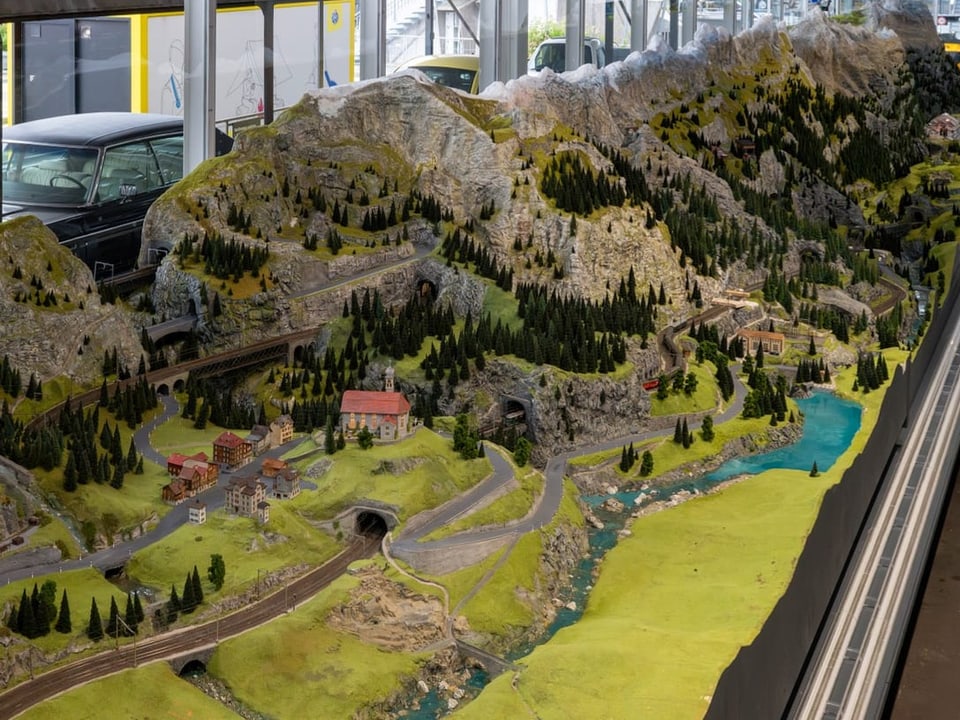 Miniaturlandschaft mit Bergen, Fluss und Modellautos im Vordergrund.