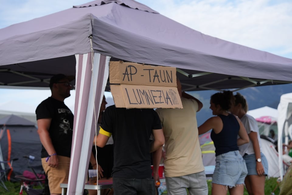 Personengruppe unter einem Zelt mit einem handgemalten Schild.